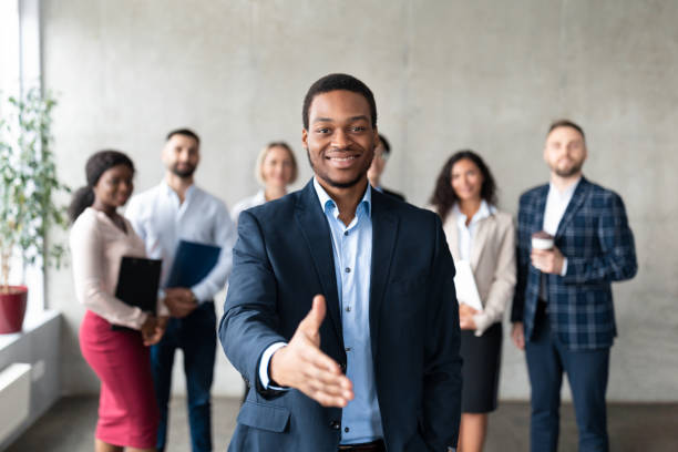 Successful African American Businessman Stretching Hand For Handshake In Office Employment. Successful African American Businessman Stretching Hand For Handshake Greeting Standing With Employees Team In Modern Office, Smiling To Camera. Career Offer Concept. Selective Focus employee introduction stock pictures, royalty-free photos & images