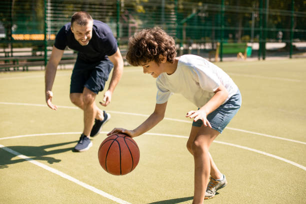 papà sportivo che insegna a suo figlio come giocare a basket fuori - basketball child dribbling basketball player foto e immagini stock