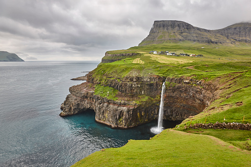 Waterfall and cliffs in Vagar. Faroe Islands dramatic coastline. Gasaladur