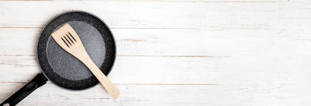 istock Frying pan with non-stick ceramic coating and spatula on a white wooden background. Cooking without sticking or oil. Banner 1315141583