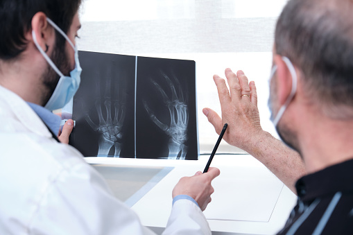 Young doctor examining x-ray of hands of a senior patient with arthritis. Radiography of a hand.