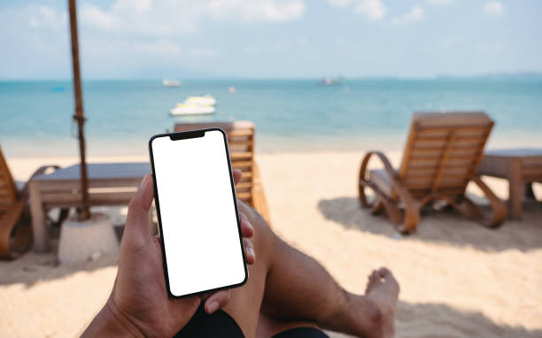 istock a man holding mobile phone with blank desktop screen while sitting on the beach 1315149949