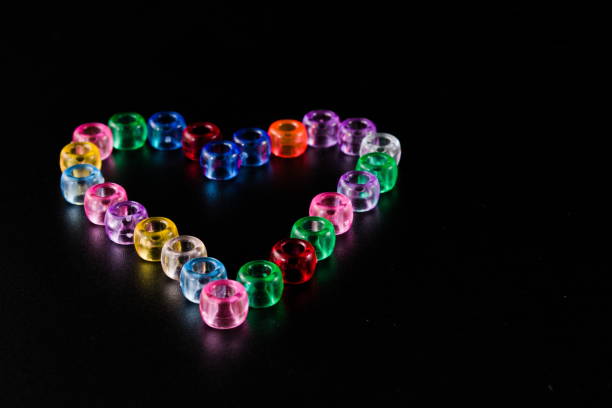 Colourful transparent beads, reflection, glow, arranged in heart shape isolated on black background