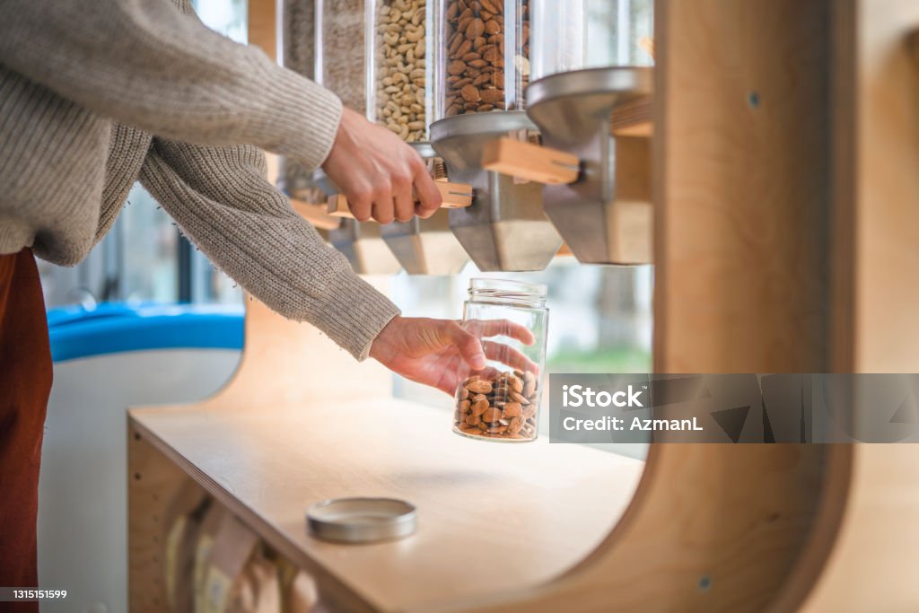 Close Up Of Using A Dispenser For Refilling In A Sustainable Plastic Free Shop Close up of a dispenser filled with nuts in a sustainable plastic free shop. Hispanic woman refilling her jar with nuts. Zero Waste Stock Photo