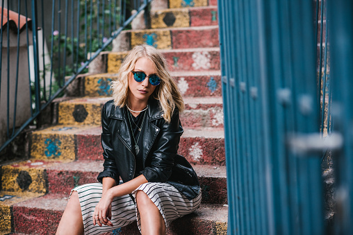 A young and beautiful modern blondie in a black leather jacket, striped pants and sunglasses, contemplating