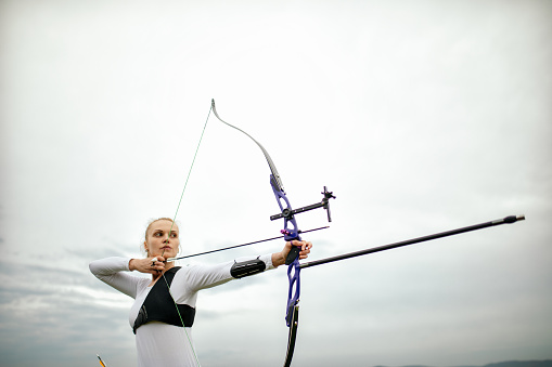 Woman practicing archery training with recurve bow on open field.