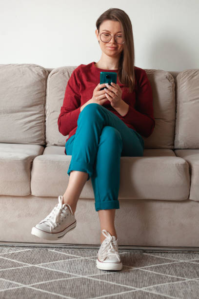 istock Woman using mobile phone, holding in hands sitting on sofa 1315154140