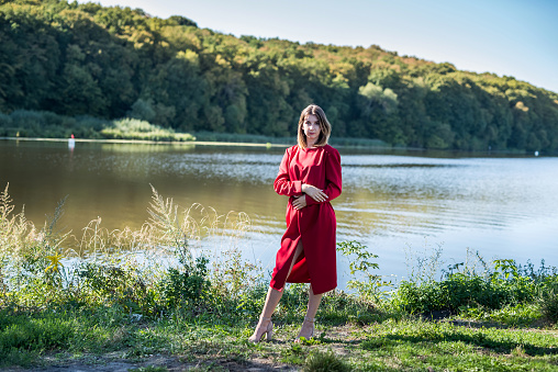 pretty woman in dress was standing by the lake, relax at nature and poses for the camera