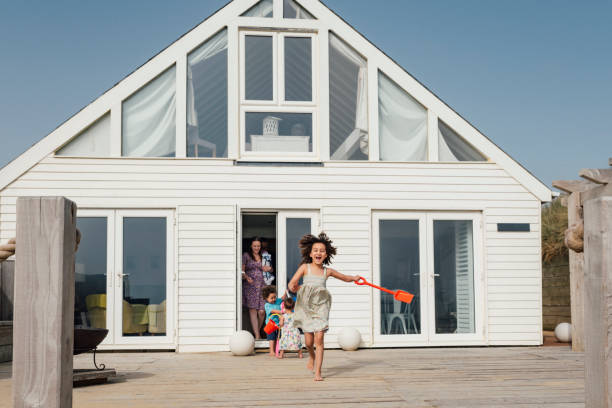 Mixed race elementary age girl leading family to the beach Full length front view of energetic young family exiting vacation home back door and heading across deck with sand pail and shovel. vacation rental stock pictures, royalty-free photos & images