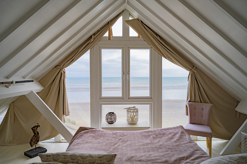 Minimalist furnishings in unoccupied A-frame design bedroom with windows and springtime view of Rye Bay on southeast coast of England.