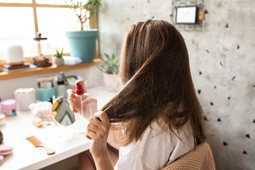 Young woman using hair spray in bedroom early in the morning