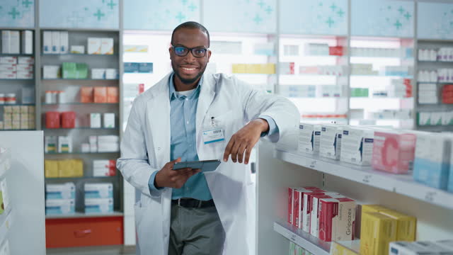 Pharmacy: Portrait of Professional Confident Black Pharmacist Uses Digital Tablet Computer, Checks Inventory of Medicine, Looks at Camera and Smiles Charmingly. Drugstore with Health Care Products
