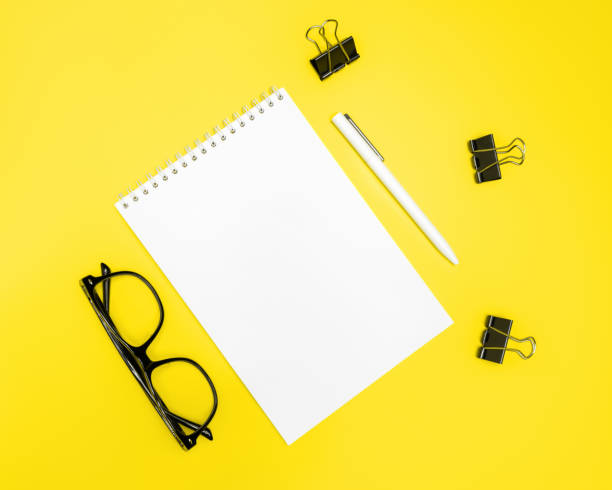 istock Notepad, pen, glasses and binder clips on yellow background. Flat lay, top view, copy space. 1315159082