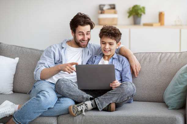 istock Caring daddy teaching son to use laptop or browsing internet together, sitting on comfy sofa in living room 1315159190