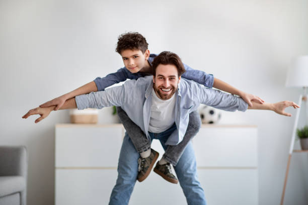 istock Playful father and son having fun together, daddy riding boy on back like flying on plane at home in living room 1315159235