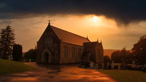 Photo of Dramatic photo of an irish country church with its cemetery next to it during a stormy sunset