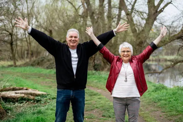 Elderly couple standing in nature spreading their arms wide open