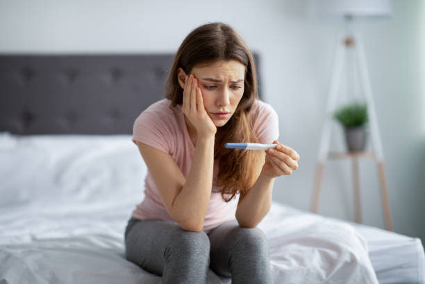 Sad young woman checking her recent pregnancy test, sitting on bed at home Sad young woman checking her recent pregnancy test, sitting on bed at home. Upset millennial lady facing unwanted childbearing or being unable to conceive baby, having maternity problem unwanted pregnancy stock pictures, royalty-free photos & images