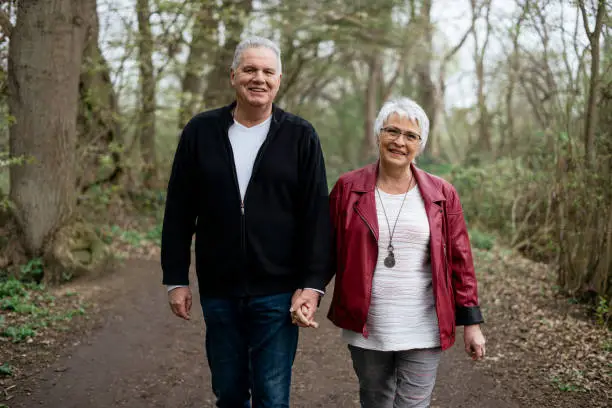 Elderly couple taking a walk in the forest and smiling at the camera