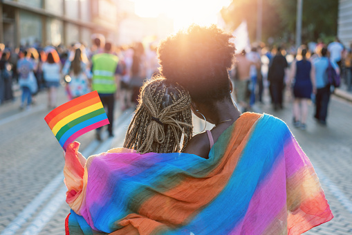 Rear view image of young couple walking with the pride event, hugging and waving pride flags
