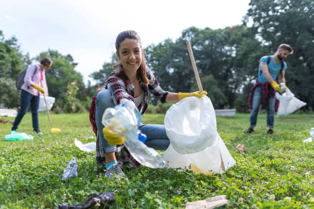 young woman picking up litter thrown away in the park - sustainable resources environment education cleaning imagens e fotografias de stock