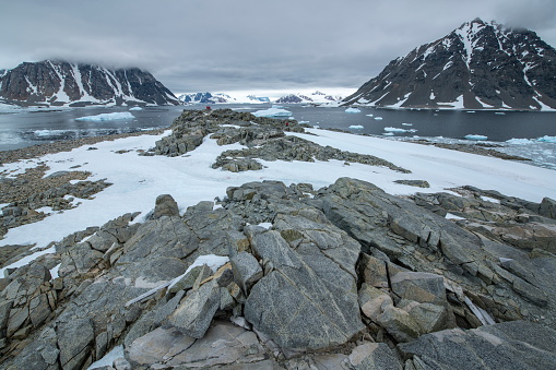 Rocks and snow cover the peninsula, with a body of water with icebergs and two mountains in the distance, Stonington Island, Antarctic Peninsula, Antarctica