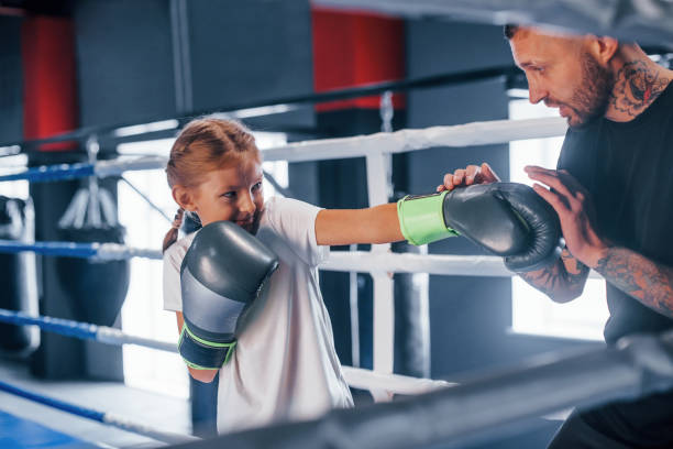 istock Having sparring with each other on the boxing ring. Young tattooed boxing coach teaches cute little girl in the gym 1315179421