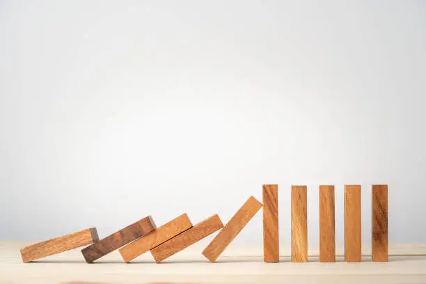 Photo of Many wooden block dominoes falling to one wooden block standing , resistance and stop risk management concept.