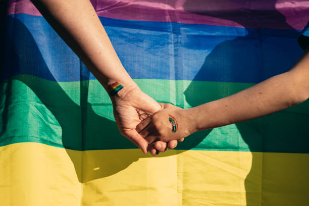 虹の旗の前で手をつないでいる母と娘 - homosexual rainbow gay pride flag flag ストックフォトと画像