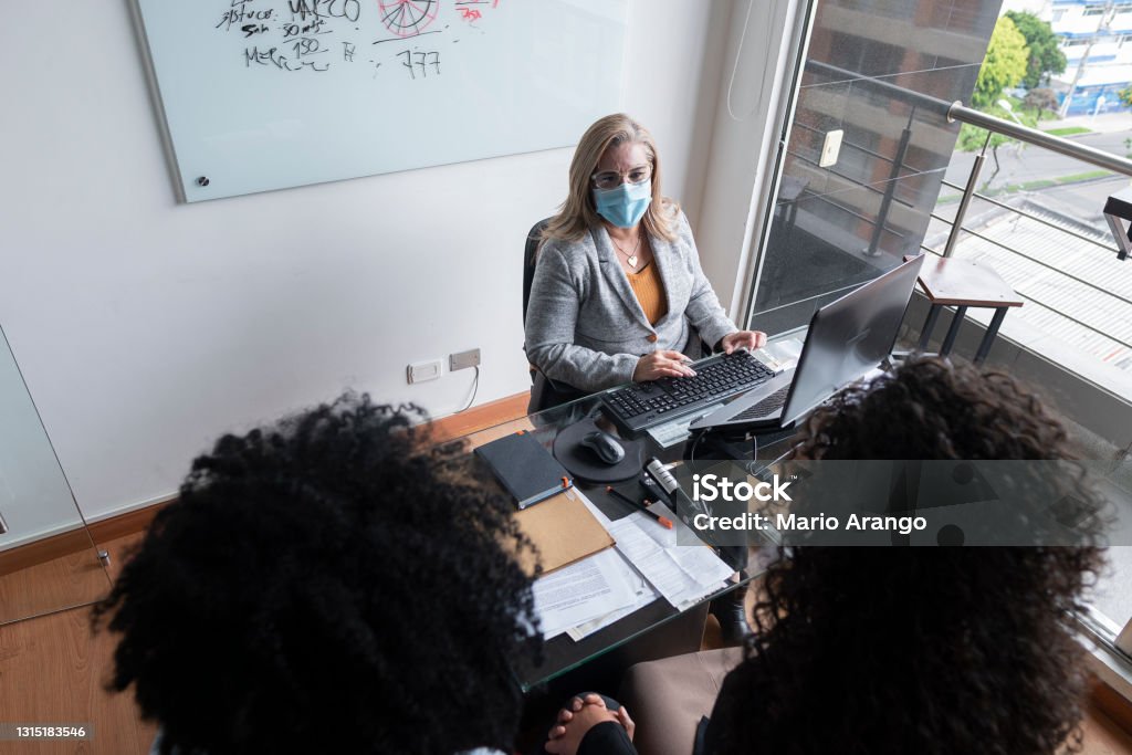 Young couple is with the bank advisor handing over the loan papers and thus buying their new house Young couple is with the bank advisor handing over the loan papers and thus buying their new house while wearing their covid 19 masks in the office Adults Only Stock Photo