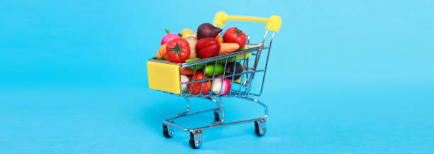 carrito de la compra de metal con frutas y verduras sobre un fondo azul. carrito de compras en miniatura de juguete - red potato raw potato market red fotografías e imágenes de stock