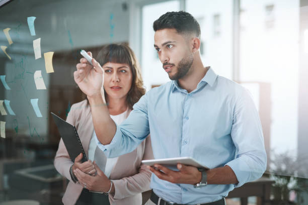 Shot of a young businessman and businesswoman using a digital tablet during a brainstorming session in a modern office Today sticky notes, tomorrow money notes transparent wipe board stock pictures, royalty-free photos & images