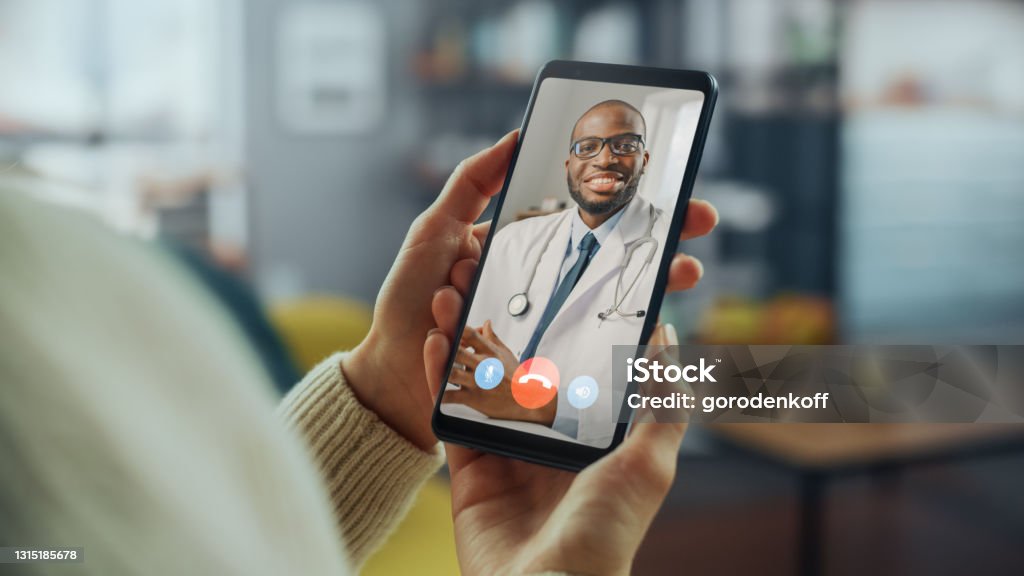 Close Up of a Female Has a Video Call with Her Female Family Doctor on Smartphone from Living Room. Ill-Feeling Woman Making a Call from Home with Physician Over the Internet. Telemedicine Stock Photo