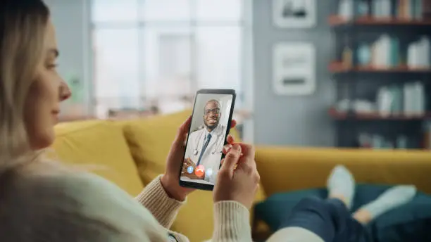 Close Up of a Female Chatting in a Video Call with Her Black Male Family Doctor on Smartphone from Living Room. Ill-Feeling Woman Making a Call from Home with Physician Over the Internet.