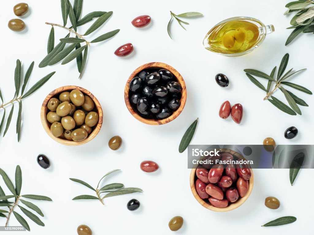 set of olives and olive oil on white background Set of green olives, black olives and red kalmata olives and extra virgin olive oil on white background. Top view of different types of olives in bowls and oil on leaves and branches background. Kalamata Olive Stock Photo