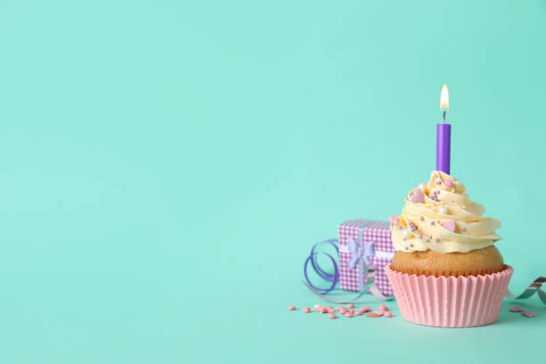 istock Birthday cupcake with burning candle, gift box  and sprinkles on turquoise background. space for text 1315193648
