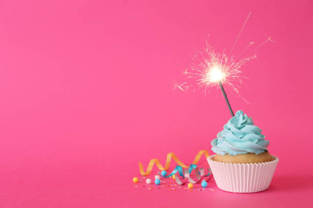 istock Birthday cupcake with burning sparkler and streamers on pink background. Space for text 1315193708