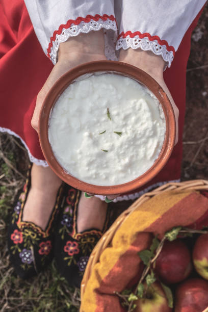 девушка, одетая в традиционный народный костюм, держит глиняный горшок с йогуртом - bulgarian culture bulgaria traditional culture food стоковые фото и изображения