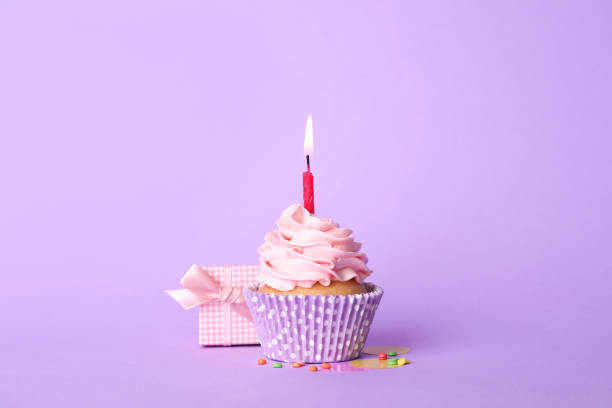istock Birthday cupcake with burning candle and gift box on violet background 1315194915