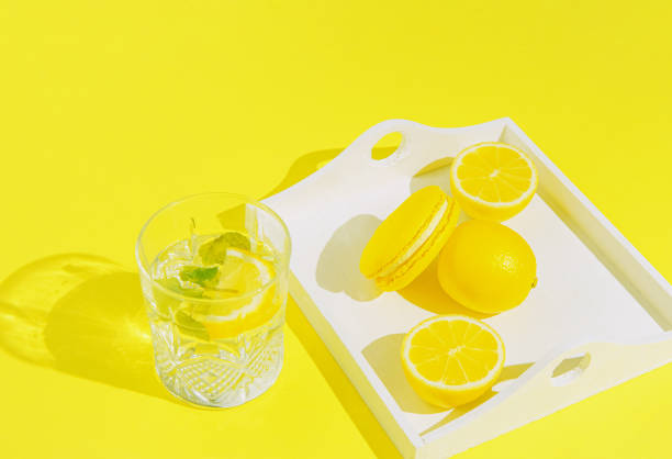 Yellow macaroon with lemons on white tray and glass of lemonade on sulit background . Summer refreshment concept.