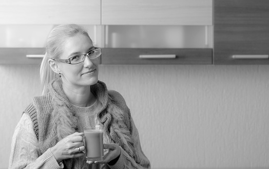 Portrait of a beautiful mid-age woman in glasses with a cup of coffee. Attractive and happy blonde in sweater drinks a latte.