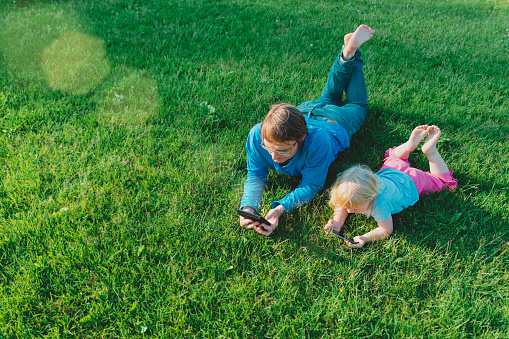 father and little daughter looking at mobile phone on green grass, summer weekend activities