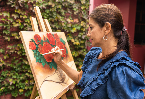 woman painting a picture on a frame on a wooden lectern outdoors