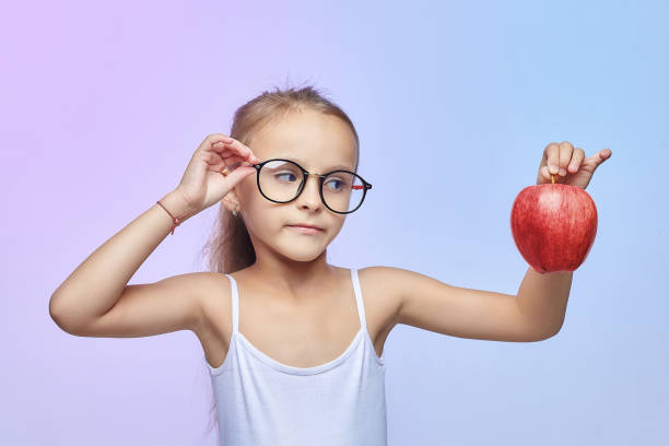 赤いリンゴを持つ眼鏡をかけた小さな女の子 - glasses child red hair little girls ストックフォトと画像