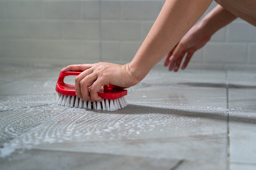 Action of a human's hand is using floor brush to cleaning toilet marble tile floor. Close-up and selective focus at hand part.