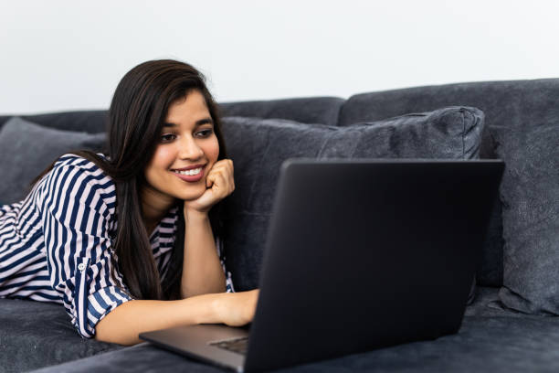istock Young indian woman using a laptop while relaxing on the couch 1315206891