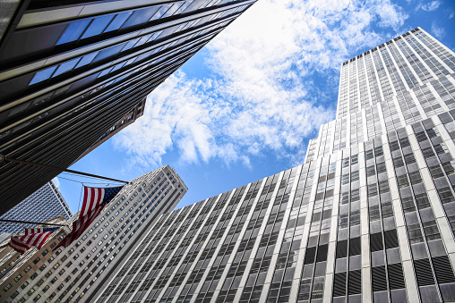 Low angle view of American flag and skyscrapers against sky in New York City. Finance, business and technology background