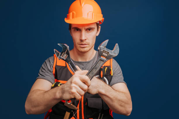 istock Smiling builder in a helmet crossed wrenches, isolated over blue background 1315208577