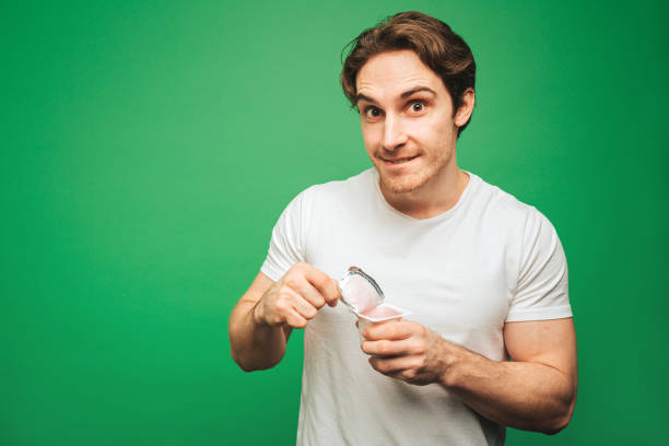 istock Young man opens yogurt with interest, isolated on green background 1315208888