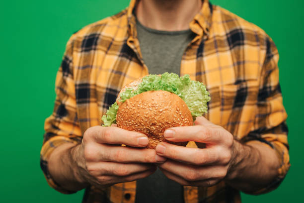 Close up young man holds burger, isolated on green background